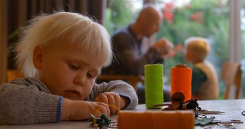 Curious Child Playing at Home with Father and Sibling in Background