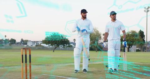 Two cricketers walking between overs holding bats on suburban cricket ground at dusk
