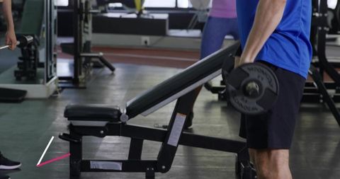 Man lifting dumbbell by incline bench at gym for strength training and muscle building
