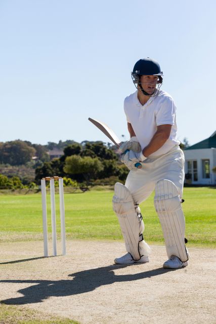 Cricket player in action on a sunny day, wearing full protective gear and helmet, ready to bat on the pitch. Ideal for use in sports-related content, articles about cricket, athletic training materials, or promotional materials for cricket events and tournaments.