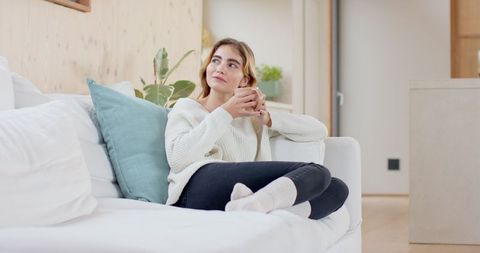 Relaxed Woman with Mug Sitting on White Sofa in Modern Living Room
