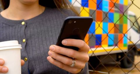 Woman holding smartphone and coffee by colorful delivery truck
