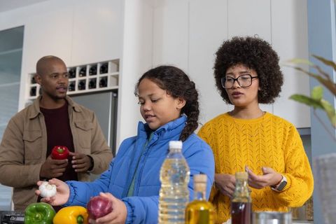 Family preparing healthy meal together in modern kitchen, child learning to cook
