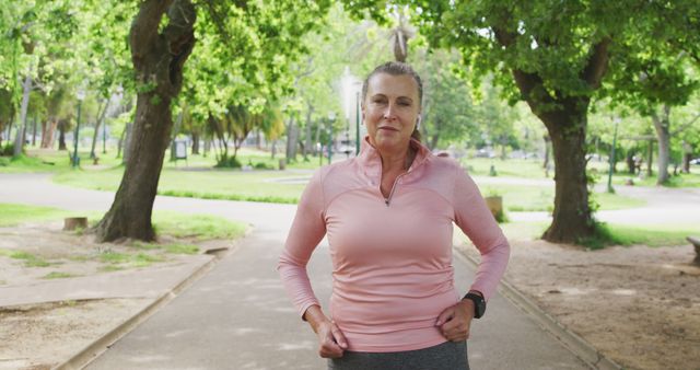 A senior woman with a determined expression jogging in a lush, green park, promoting an active and healthy lifestyle. Perfect for material related to active aging, fitness and exercise tips, health and wellness campaigns, outdoor activity promotions, and senior health improvement. Can be used for brochures, websites, and ads focusing on seniors maintaining physical fitness and enjoying nature.