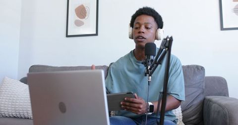 Young podcaster recording from home studio with laptop, tablet and professional microphone