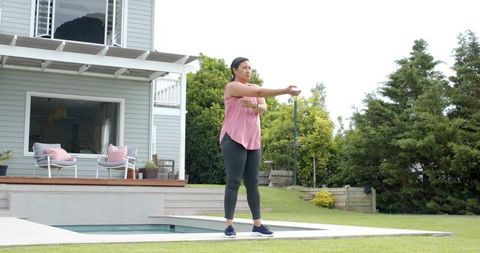 Mature woman stretching arm by plunge pool on contemporary backyard deck morning routine