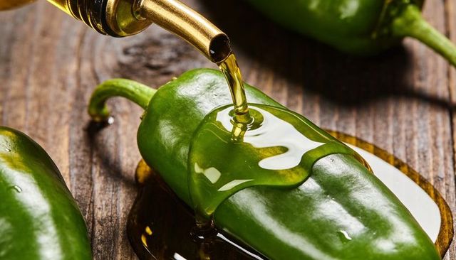 Olive oil pouring over jalapeno pepper closeup on rustic wood surface, glossy green pepper