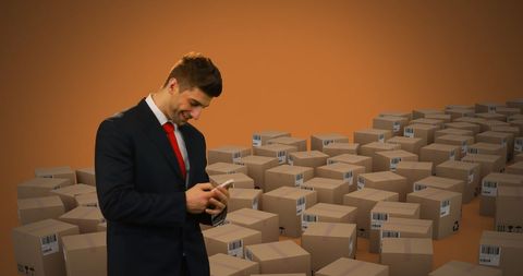 Businessman using smartphone in warehouse with cardboard boxes