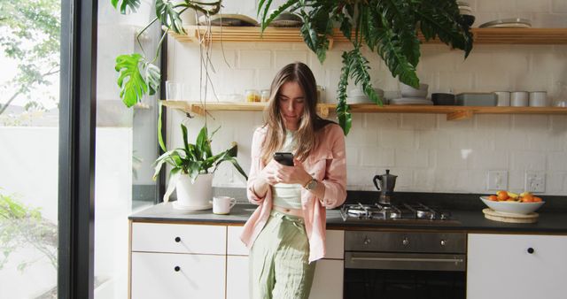 Caucasian non-binary transgender woman using smartphone in kitchen. spending quality time at home alone, body inclusivity.