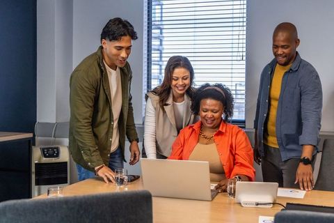 Diverse team collaborating around laptop in modern conference room with charts