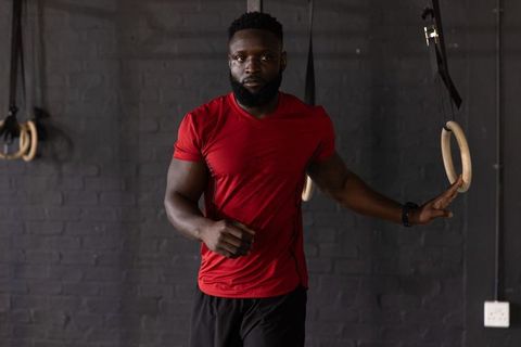 African american athlete resting hand on gym rings wearing red shirt training strength