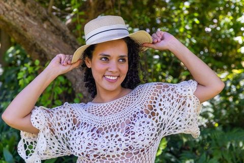 African american woman smiling wearing straw hat and white crochet top in sunlit garden