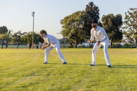 Cricket fielders standing ready on sunlit grass in white uniforms during golden hour