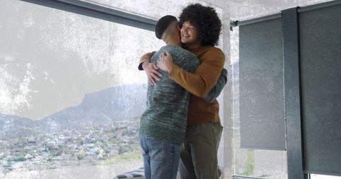 Two men embracing by panoramic window in modern apartment sharing warm hug