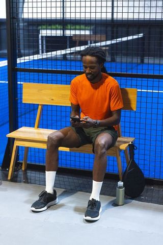 Padel enthusiast relaxed on bench checking smartphone