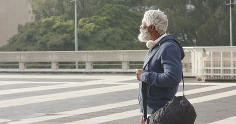 Senior African American man standing on urban plaza carrying duffel bag with headphones