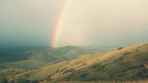 Ethereal Rainbow Illuminating Verdant Hills Under Parting Clouds
