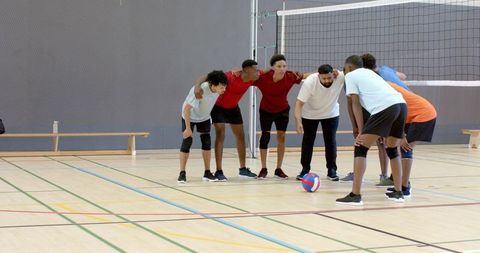 Diverse male volleyball team huddling on indoor court planning strategy and teamwork