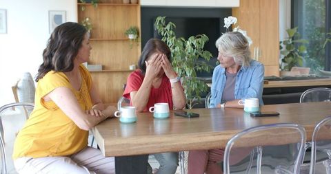 Mature women consoling friend at wooden table showing empathy and emotional support