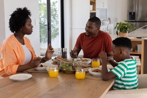 African american family sharing breakfast around wooden dining table in modern kitchen