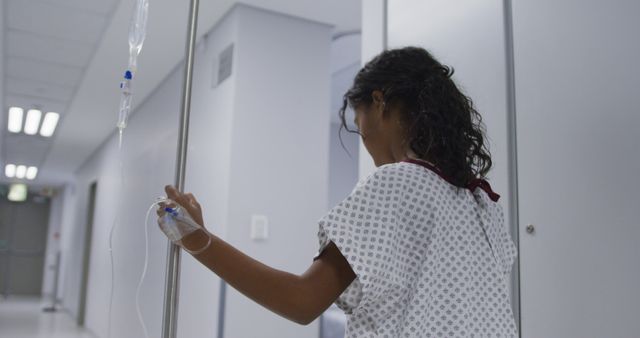 Biracial girl walking with drip bag in hospital room. medicine, health and healthcare services.