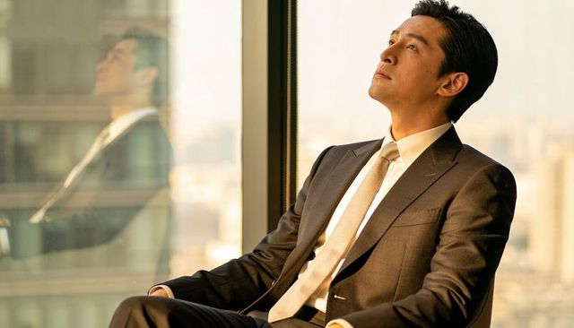 Executive contemplating by office window overlooking cityscape during golden hour
