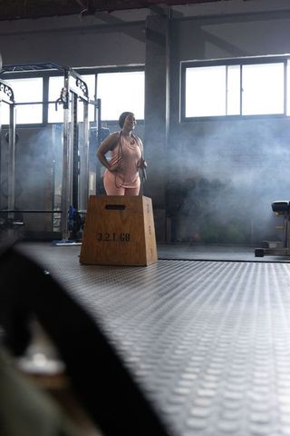 African american woman training with jump rope beside plyo box in gym sunlight haze