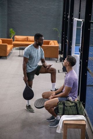 Two men pausing between padel games in modern indoor club holding paddles and phone