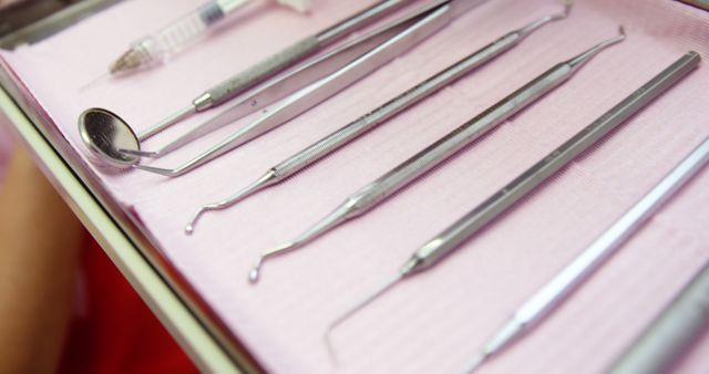 Various stainless steel dental tools, including a dental mirror, explorer, and scaler, lying on a pink cloth. Useful for illustrating dental services, professional dental care, and hygienic practices in a dentist's office.