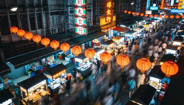 Lantern-lit night market with busy street food stalls, neon signs and motion-blur crowd