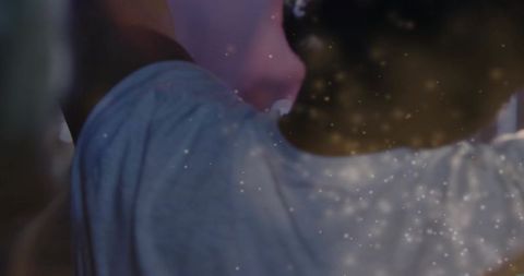 Standing man wearing loose pale t-shirt under dim club lights with glitter bokeh