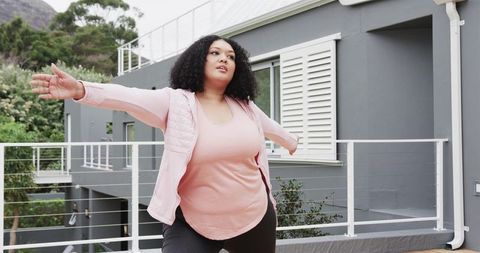 Balancing woman stretching arms on modern balcony railing wearing pale pink vest