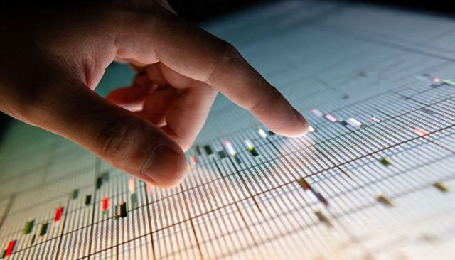 Hand interacting with touchscreen candlestick chart showing financial market data and trading