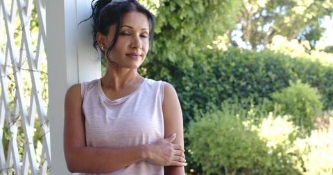 Indian woman leaning on porch column, closing eyes and relaxing in sunlit garden