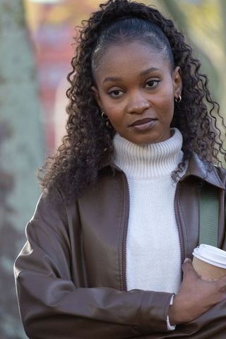 African american woman holding coffee, wearing jacket, contemplative street portrait