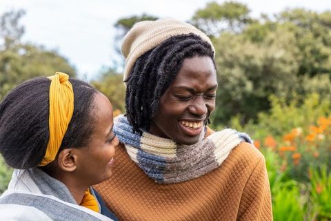 African american couple laughing and embracing in garden wearing knit beanie and scarf