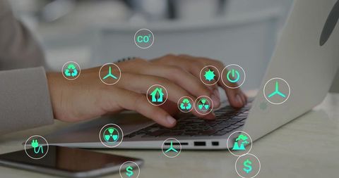 Hands typing on laptop with green sustainability icons overlay, renewable energy concept