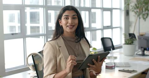 Indian businesswoman presenting with tablet in modern open-plan office, smiling confidently