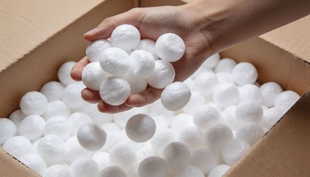 Adult right hand cupping white polystyrene foam balls over corrugated cardboard box