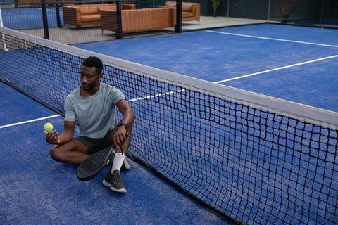 Athlete sitting at net holding paddle and ball on blue court resting between rallies
