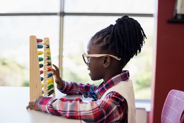 Young girl using an abacus in a classroom setting, focusing on learning math. Ideal for educational materials, school websites, and articles on childhood education and learning tools.