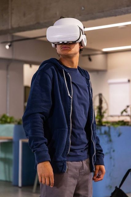 Teen wearing white vr headset and navy hoodie in modern coworking space looking up