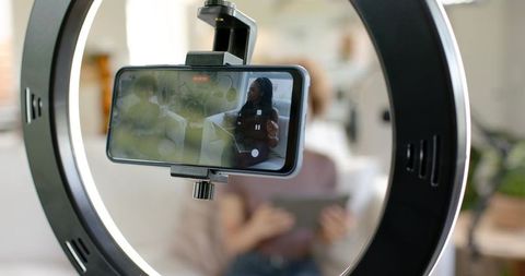 African american women hosting live stream on smartphone with ringlight in home studio