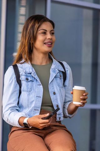 Urban commuter african american woman holding coffee and checking phone in denim jacket