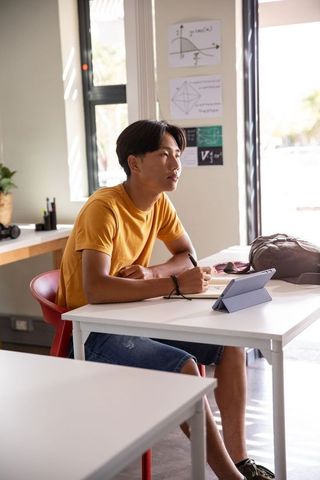 Teenage asian student studying with tablet and notebook in bright study space