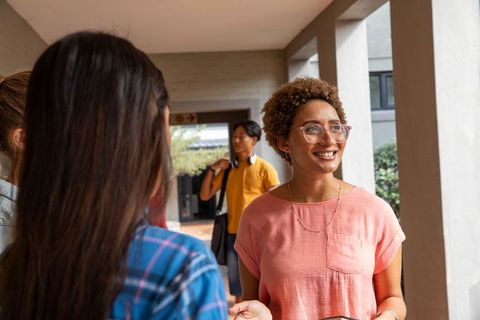 Smiling young woman chatting with friends while walking through college campus walkway