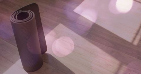 Standing rolled dark yoga mat casting long shadow on wood floor with window light bokeh