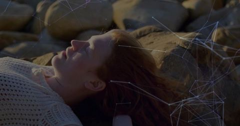 Woman in white top relaxing among rocks with glowing network overlay