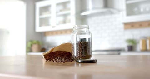 Pouring coffee beans into jar on kitchen counter