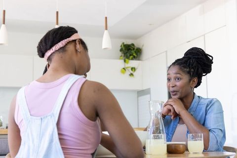 African mother and teenage daughter sharing morning conversation at kitchen breakfast bar